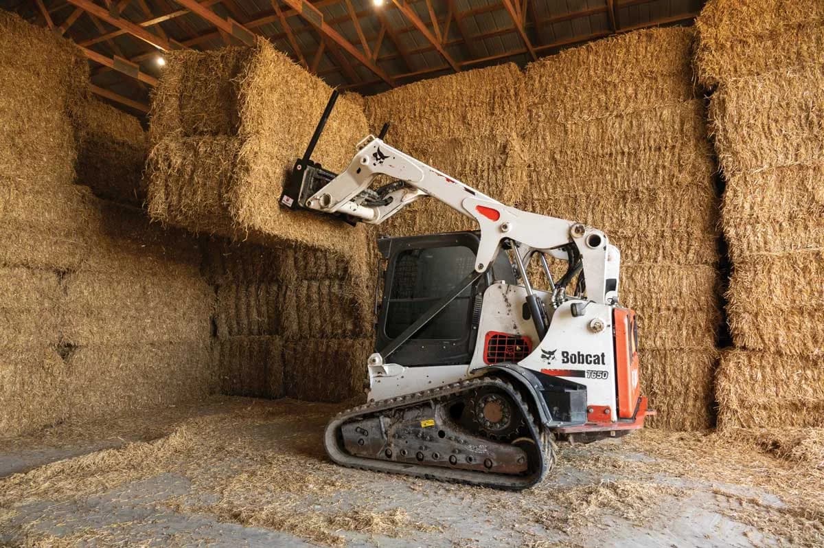 Skid steer with bale spear stacking hay in the barn