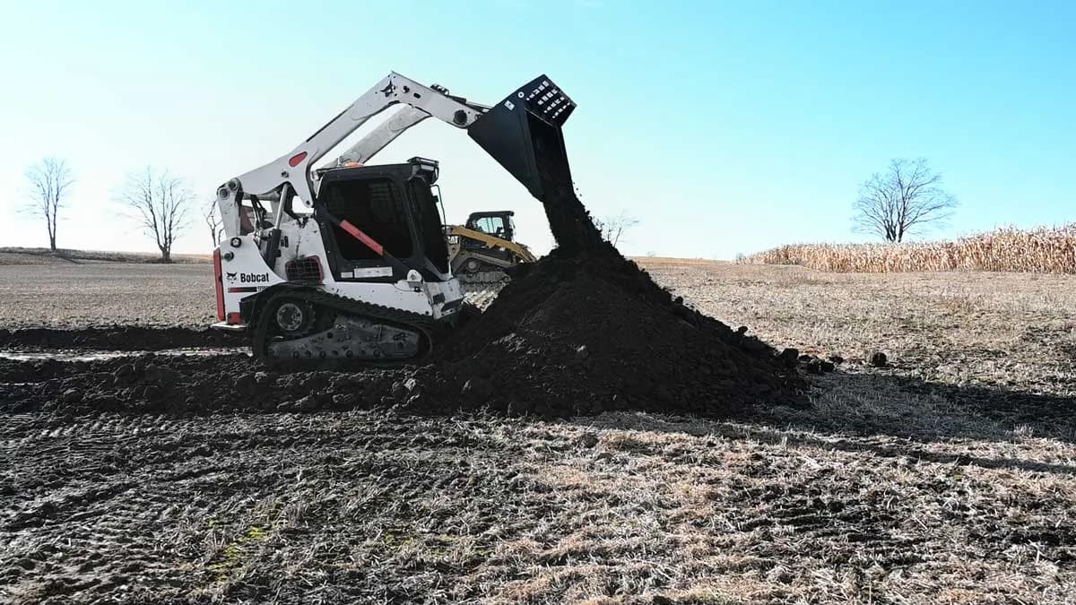 Skid steer dumping a bucket of topsoil